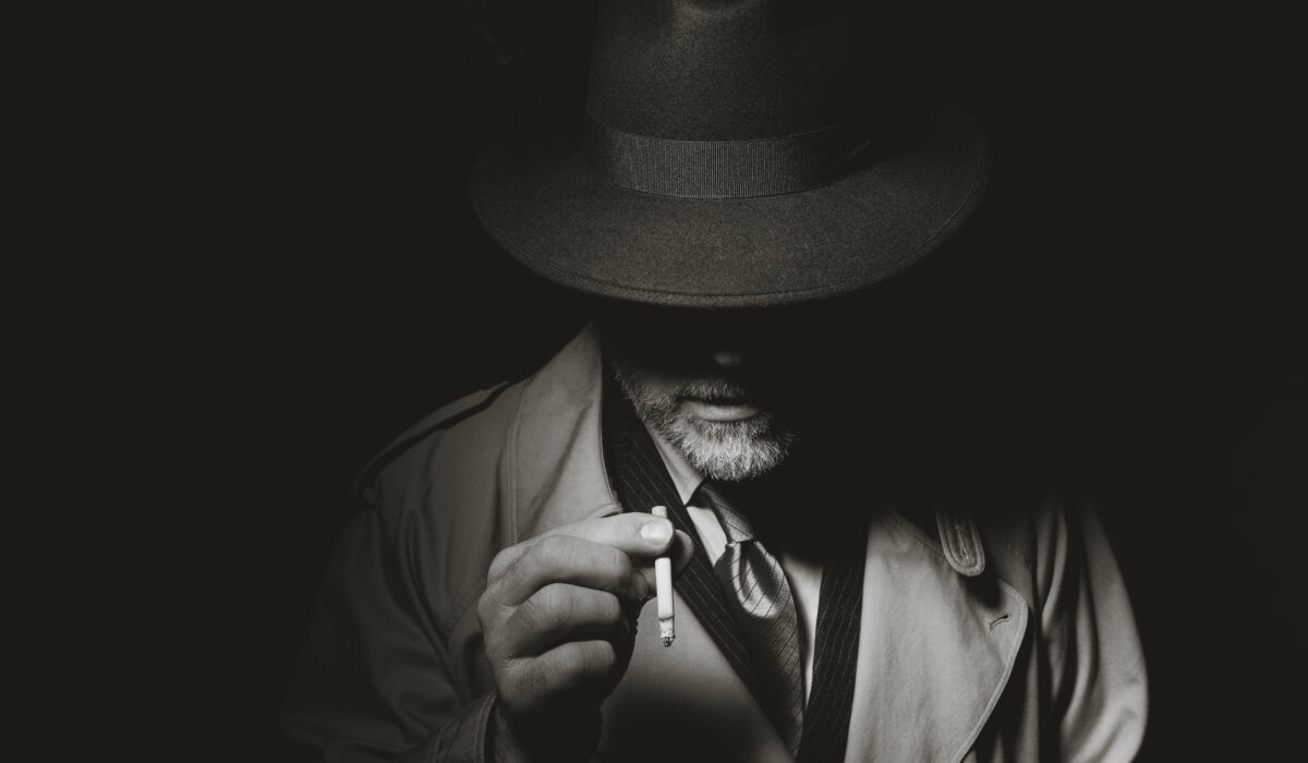 Noir film character standing in the dark and smoking a cigarette, he is wearing a fedora hat and a trench coat